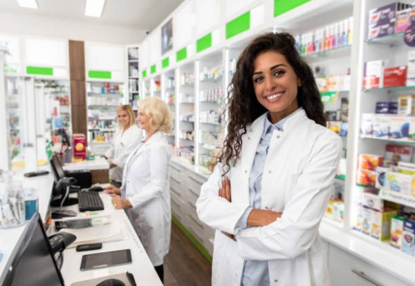 Pharmacienne souriante en blouse blanche dans une pharmacie au Québec, illustrant le rôle essentiel des pharmaciens auprès des patients