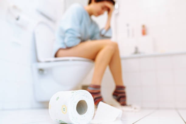 Femme assise aux toilettes souffrant de constipation, rouleau de papier hygiénique au sol