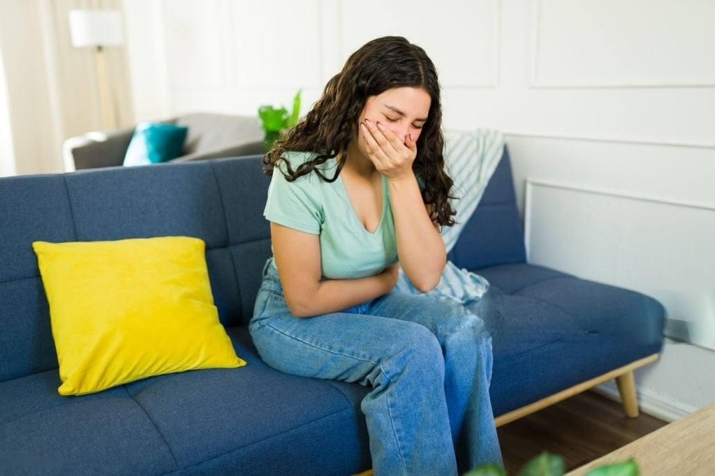 Femme assise sur un canapé souffrant de nausées et se tenant le ventre