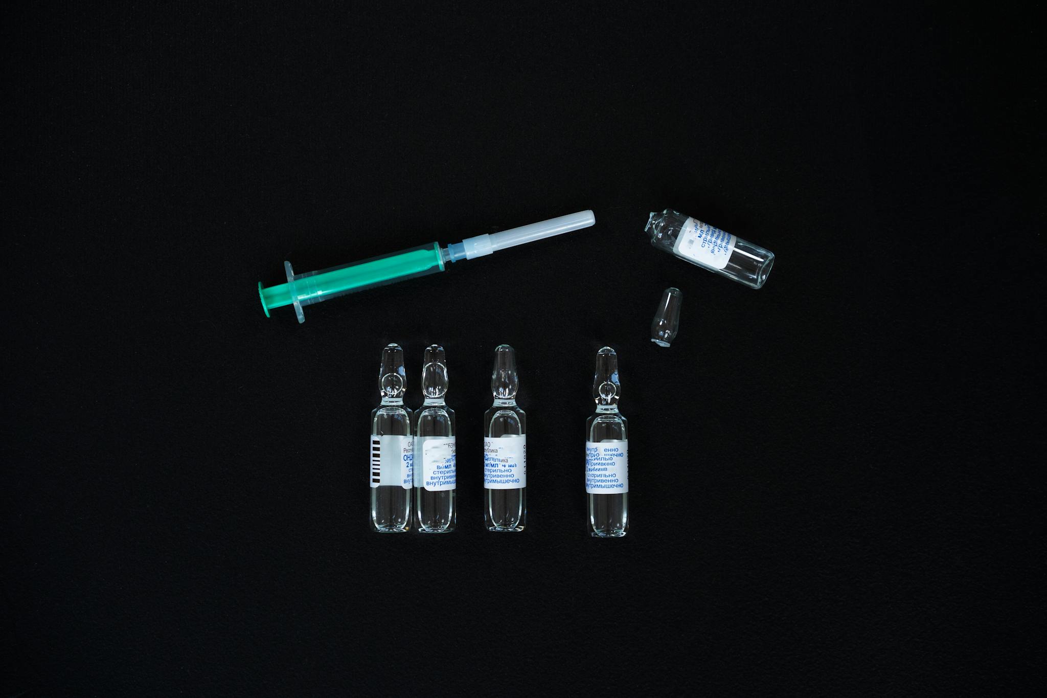 A close-up view of glass ampoules and a syringe on a black background, representing medical supplies.