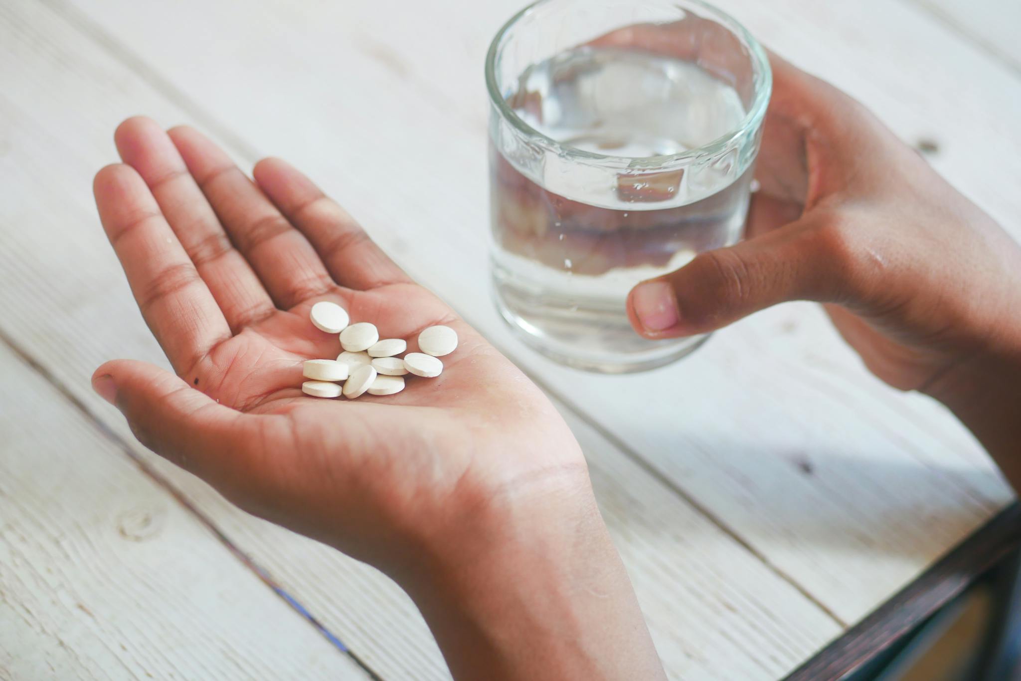 Close-up of hands holding pills and a glass of water, symbolizing medication intake.