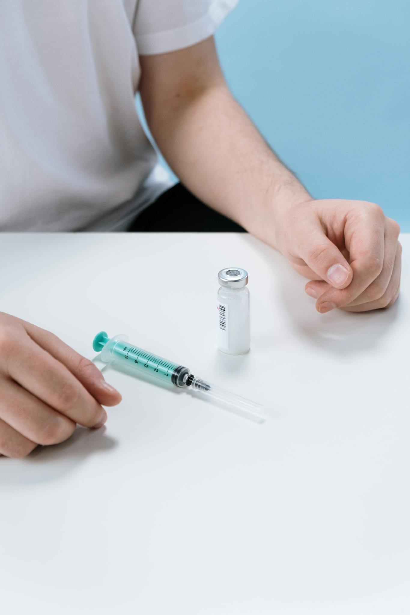 Close-up of hands with a syringe and vial on a white surface, representing medical care.
